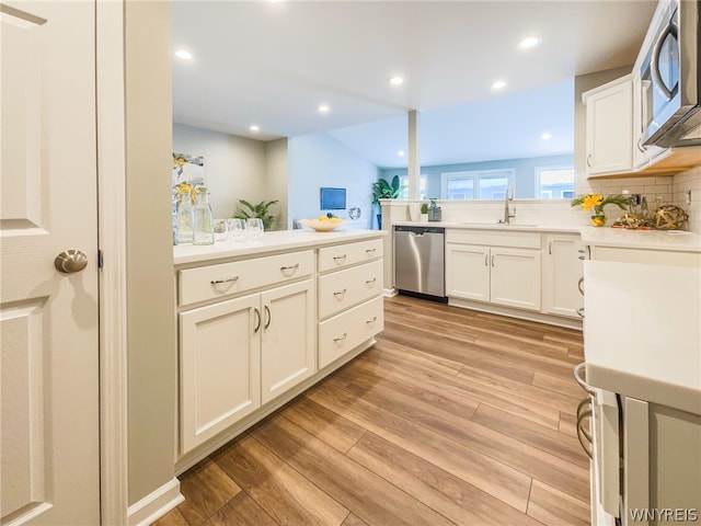 kitchen featuring backsplash, sink, light wood-type flooring, kitchen peninsula, and stainless steel appliances