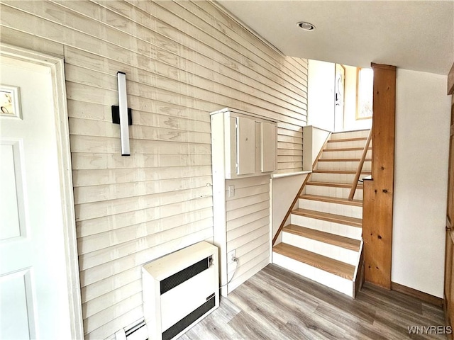 stairway featuring wood-type flooring, heating unit, and wooden walls