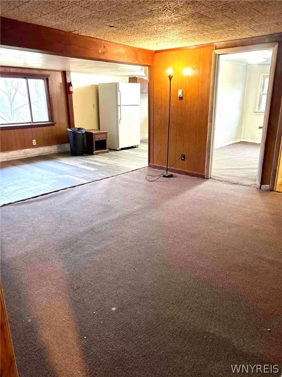 interior space with light carpet, beamed ceiling, and wood walls