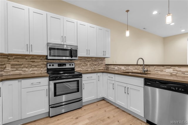 kitchen with hanging light fixtures, light hardwood / wood-style flooring, appliances with stainless steel finishes, backsplash, and sink