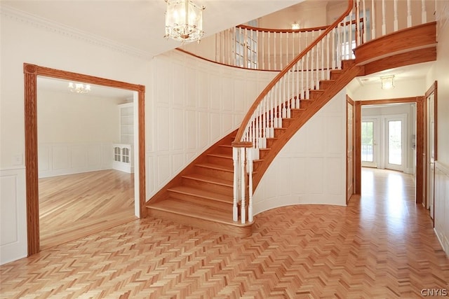 staircase featuring parquet flooring, ornamental molding, and a notable chandelier