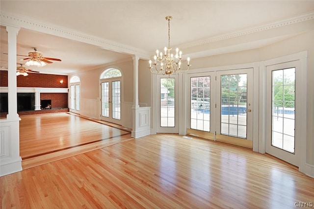 interior space with ceiling fan with notable chandelier, light wood-type flooring, a brick fireplace, and crown molding