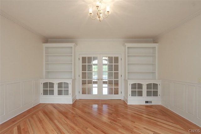 unfurnished room featuring french doors, built in shelves, crown molding, and a notable chandelier