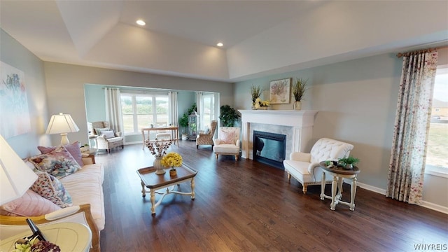 living area featuring recessed lighting, dark wood-type flooring, a high end fireplace, baseboards, and a tray ceiling