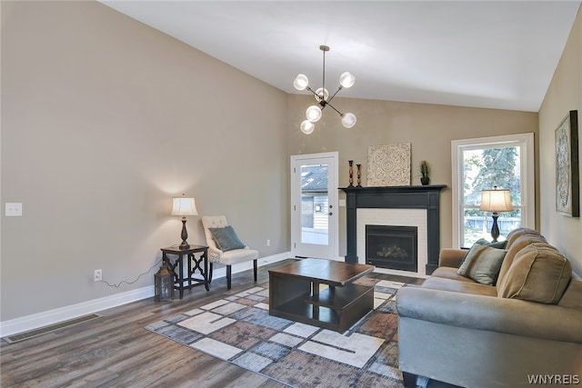 living room featuring a brick fireplace, hardwood / wood-style flooring, lofted ceiling, and an inviting chandelier