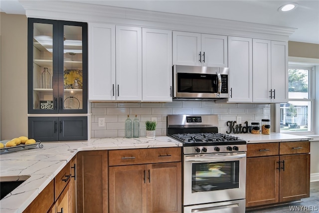 kitchen featuring backsplash, white cabinetry, light stone countertops, and stainless steel appliances