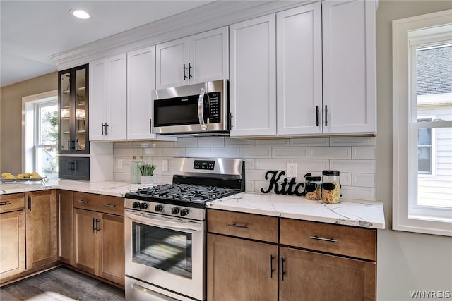 kitchen featuring hardwood / wood-style floors, tasteful backsplash, light stone counters, white cabinetry, and stainless steel appliances