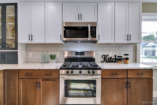 kitchen with backsplash, light stone counters, white cabinetry, and appliances with stainless steel finishes