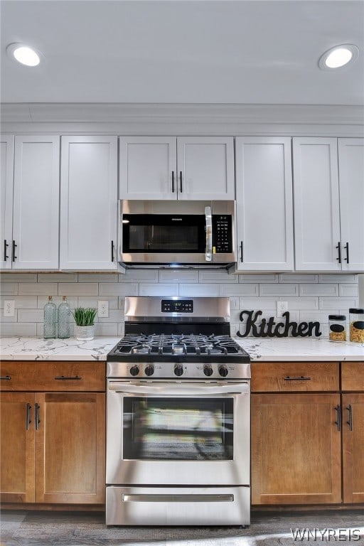 kitchen featuring decorative backsplash, light stone counters, white cabinetry, and appliances with stainless steel finishes