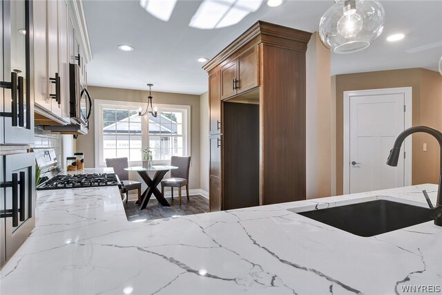 kitchen featuring backsplash, light stone counters, sink, pendant lighting, and an inviting chandelier