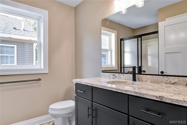 bathroom with vanity, toilet, a shower with shower door, and a wealth of natural light