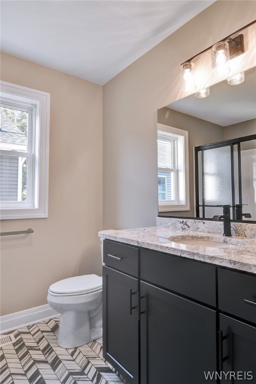 bathroom featuring an enclosed shower, vanity, toilet, and a wealth of natural light