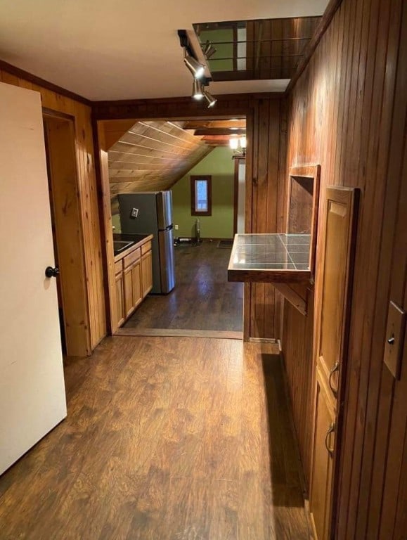 kitchen featuring vaulted ceiling with beams, stainless steel fridge, dark hardwood / wood-style flooring, and wood walls