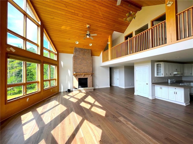 unfurnished living room featuring high vaulted ceiling, dark hardwood / wood-style floors, ceiling fan, a fireplace, and beam ceiling