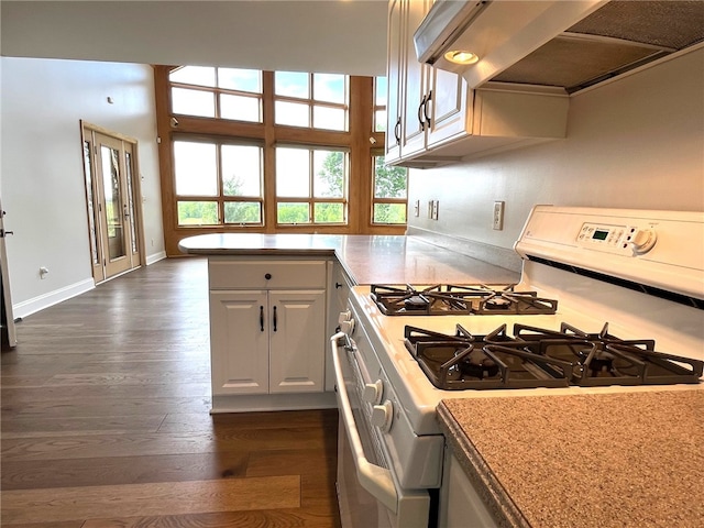 kitchen with kitchen peninsula, white gas range oven, extractor fan, white cabinets, and dark hardwood / wood-style floors