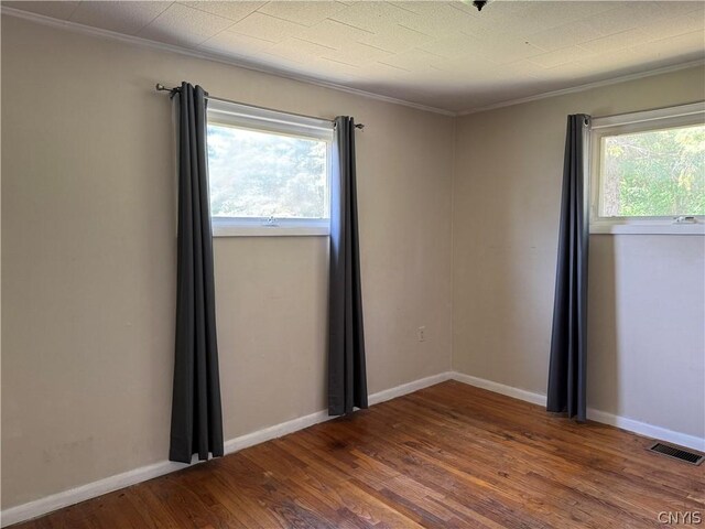 empty room with hardwood / wood-style floors, crown molding, and a wealth of natural light