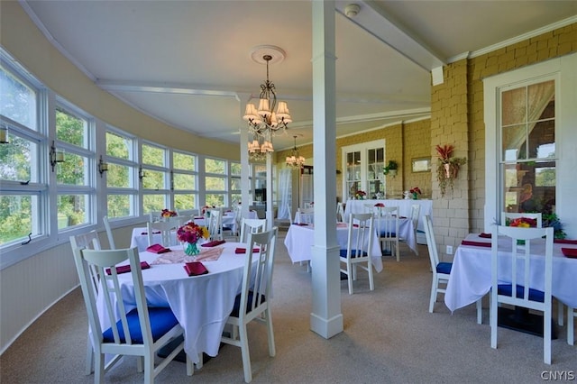 dining area with a notable chandelier, beam ceiling, ornamental molding, and brick wall