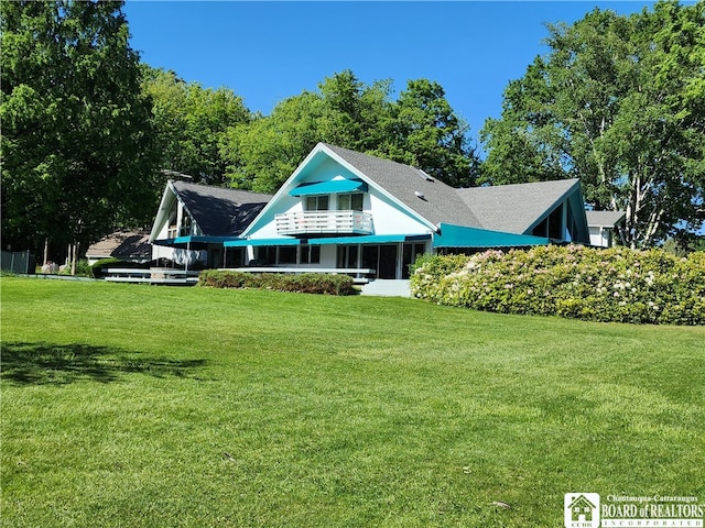 rear view of property featuring a balcony and a lawn