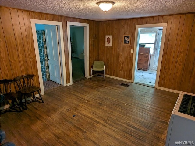 empty room with dark wood-type flooring, a textured ceiling, and wood walls