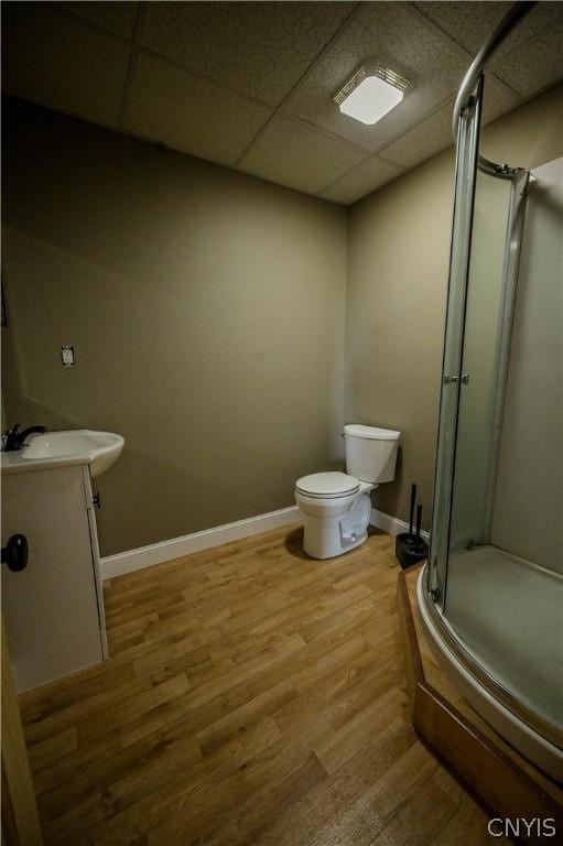 bathroom with a drop ceiling, walk in shower, toilet, vanity, and hardwood / wood-style flooring