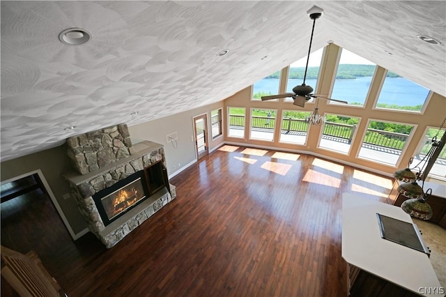 living room featuring ceiling fan, dark hardwood / wood-style flooring, vaulted ceiling, a fireplace, and a water view