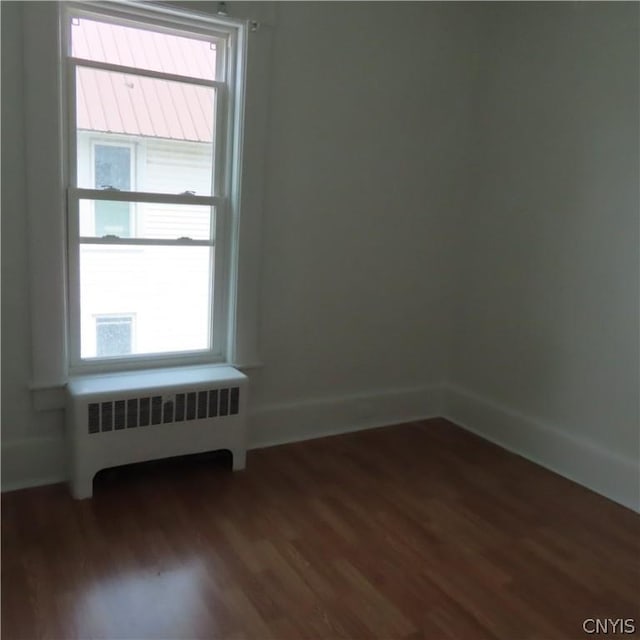 empty room with a wealth of natural light, radiator heating unit, and dark wood-type flooring