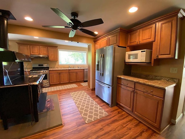 kitchen featuring stainless steel appliances, ceiling fan, sink, hardwood / wood-style flooring, and a wood stove