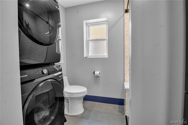 bathroom featuring stacked washer and clothes dryer, toilet, and tile patterned flooring