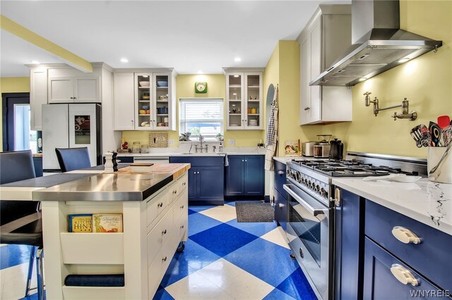 kitchen with light tile patterned flooring, white cabinetry, a breakfast bar, wall chimney range hood, and stainless steel appliances