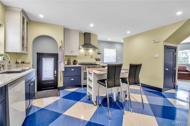 kitchen featuring light tile patterned flooring, wall chimney range hood, stainless steel appliances, blue cabinetry, and sink