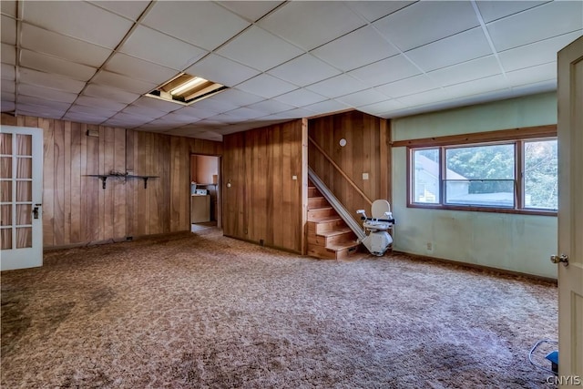 below grade area featuring stairs, wooden walls, a paneled ceiling, and carpet floors