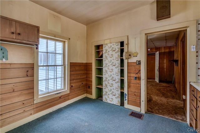 unfurnished bedroom featuring dark colored carpet, wooden walls, and visible vents