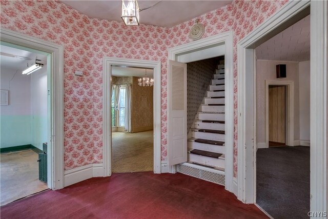 interior space with dark carpet, a chandelier, stairs, wallpapered walls, and baseboards