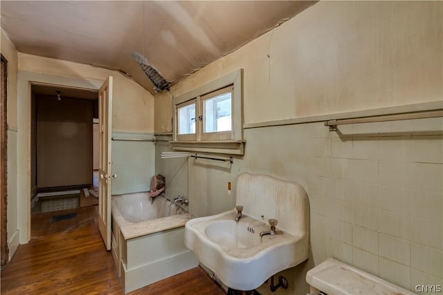 bathroom with a sink, vaulted ceiling, wood finished floors, and a garden tub