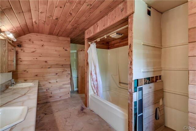 bathroom featuring concrete floors, a sink, wooden walls, shower / bathtub combination with curtain, and lofted ceiling