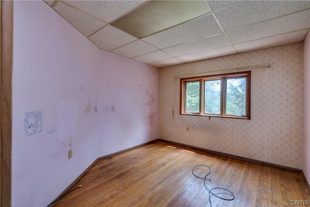 spare room featuring light wood-style flooring, wallpapered walls, baseboards, and a drop ceiling