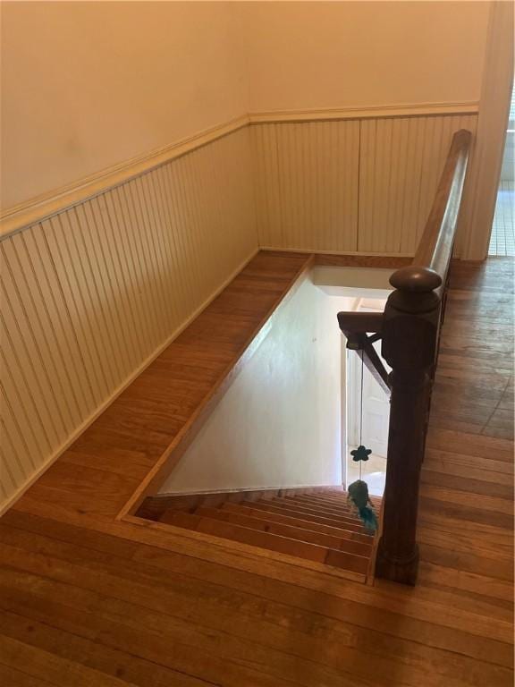 stairway with a wainscoted wall and wood finished floors