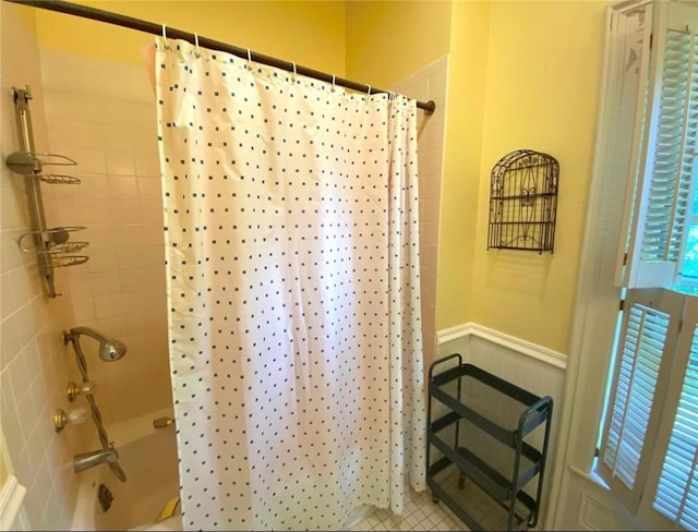 bathroom featuring a wainscoted wall and shower / bathtub combination with curtain