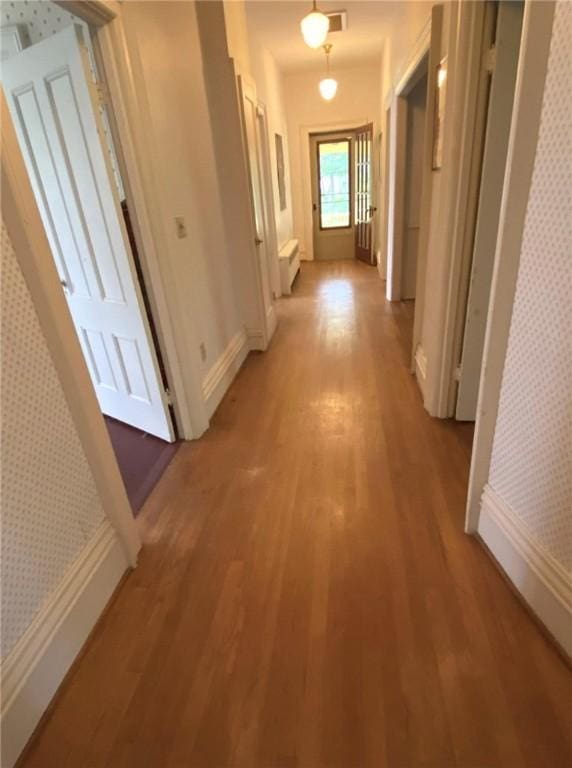 hallway with baseboards, light wood finished floors, and wallpapered walls