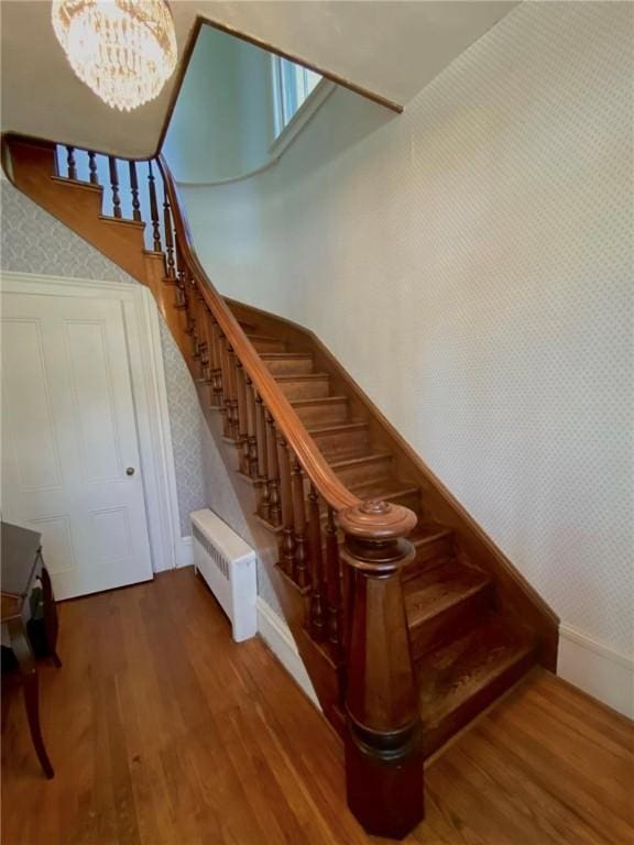 stairway featuring a notable chandelier, radiator, wood finished floors, baseboards, and wallpapered walls