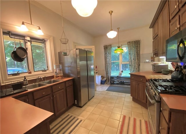 kitchen with dark brown cabinetry, light tile patterned floors, decorative light fixtures, stainless steel appliances, and a sink