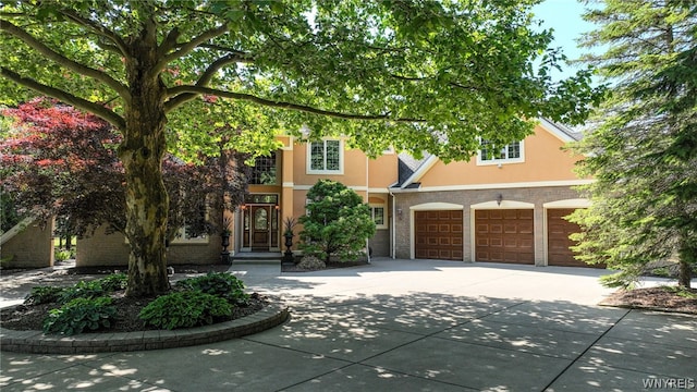 view of property hidden behind natural elements featuring concrete driveway, brick siding, and stucco siding