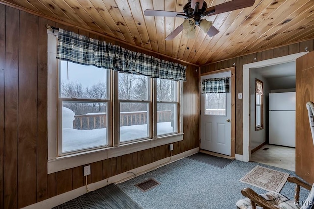 interior space featuring light carpet, wooden ceiling, ceiling fan, and wood walls