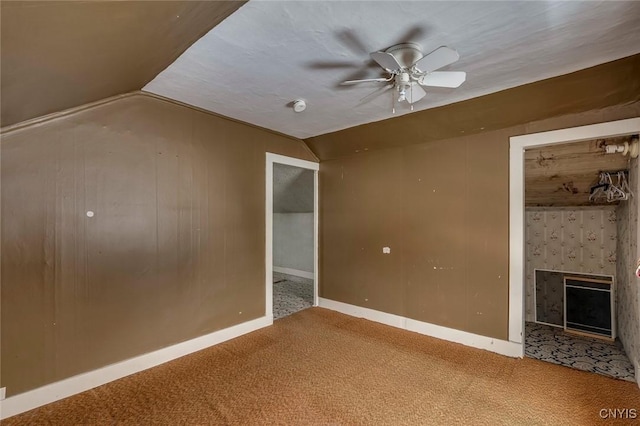 interior space with vaulted ceiling, wooden walls, ceiling fan, a fireplace, and carpet