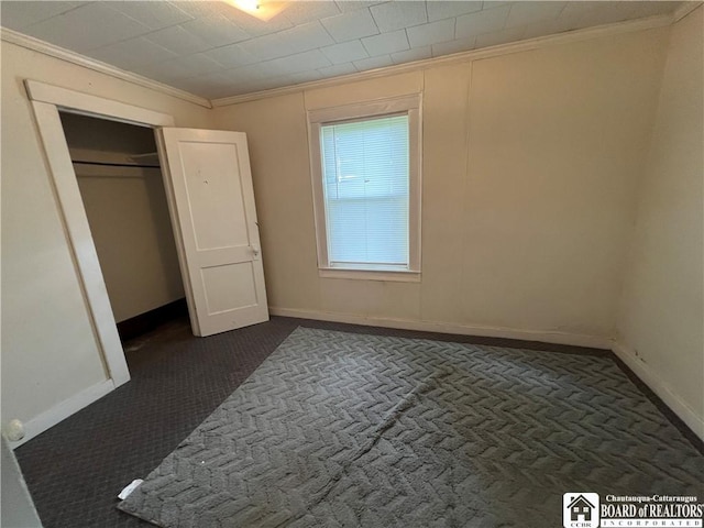 unfurnished bedroom with dark carpet, ornamental molding, and a closet