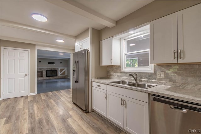 kitchen with appliances with stainless steel finishes, a brick fireplace, sink, light hardwood / wood-style floors, and white cabinetry