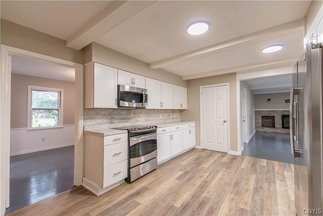 kitchen with beam ceiling, white cabinets, stainless steel appliances, and light wood-type flooring