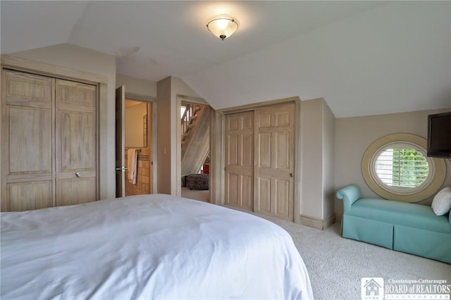 carpeted bedroom featuring vaulted ceiling and multiple closets