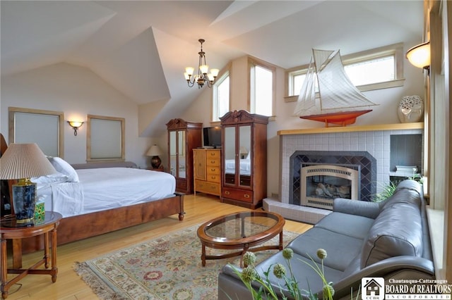 bedroom with a fireplace, lofted ceiling, light hardwood / wood-style floors, and a notable chandelier