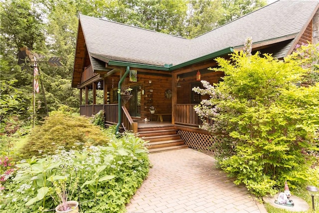 entrance to property with covered porch, a shingled roof, and a patio area